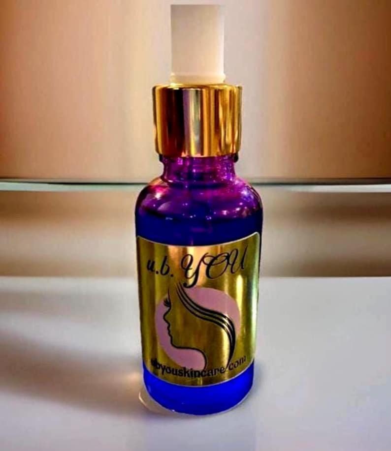 Peut inclure: Une bouteille en verre violet avec un bouchon dor&eacute; et un applicateur blanc. La bouteille porte une &eacute;tiquette dor&eacute;e avec le texte "u.b. YOU" et une silhouette de visage de femme. L'adresse du site Web byouskincare.com figure &eacute;galement sur l'&eacute;tiquette. La bouteille est remplie d'un liquide clair.