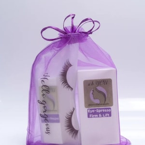 May include: A purple organza drawstring bag containing two white rectangular boxes and a pair of false eyelashes. The bag features the text Hello gorgeous in black script. The boxes are labeled ab YOU Eye-Spresso Firm & Lift in purple and white.