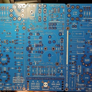 Puede incluir: Una placa de circuito azul con texto y componentes blancos. La placa está etiquetada como "TUBE Audio Power AMP EL34/KT88 PP" e incluye advertencias sobre alta tensión. Presenta varios componentes electrónicos.