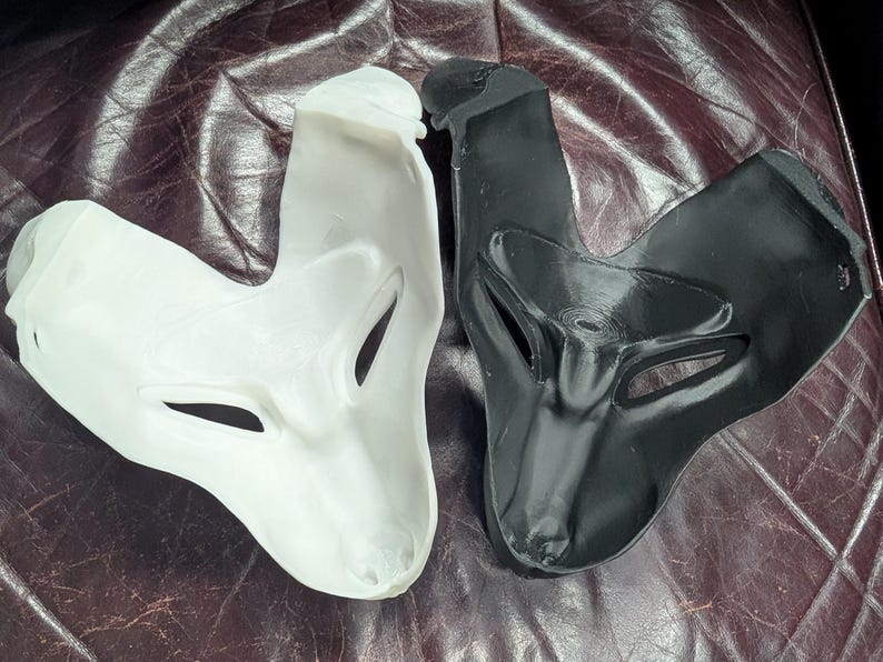 May include: Two fox-shaped masks, one white and one black, are displayed. The masks have eye and nose openings and are made of a smooth material. The masks are likely for costume or theatrical use.
