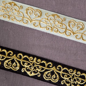 K&ouml;nnte beinhalten: Zwei dekorative B&auml;nder mit goldgestickten Designs. Ein Band ist wei&szlig;, das andere ist schwarz. Die goldene Stickerei zeigt ein sich wiederholendes Muster aus Herzen und wirbelnden Linien, das einen eleganten und verzierten Look erzeugt.