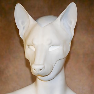 May include: A matte white, smooth-surfaced animal mask featuring tall, pointed ears and a defined snout. The mask covers the upper face, including the eye area, and is displayed on a matching white mannequin head with a neutral, clean aesthetic.