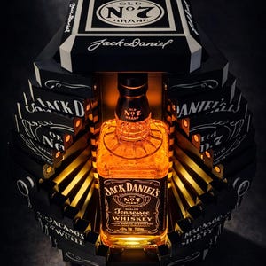 Puede incluir: Una botella de Jack Daniel's Tennessee Whiskey en una caja decorativa en blanco y negro. La botella está iluminada, mostrando el líquido ámbar y la etiqueta de la marca. La caja presenta el nombre y el logotipo de la marca.