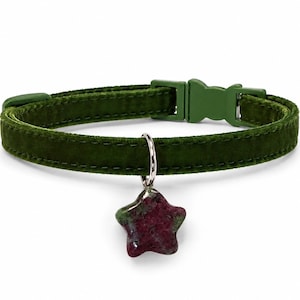 May include: A dark olive green velvet pet collar featuring a matching green plastic side-release buckle and a silver-toned metal ring. A star-shaped pendant made of mottled dark red and green stone hangs from the silver ring on the collar.