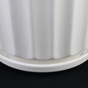 May include: A white ceramic planter with a ribbed design. The planter sits on a matching white saucer. The image is a close-up of the planter and saucer against a black background.