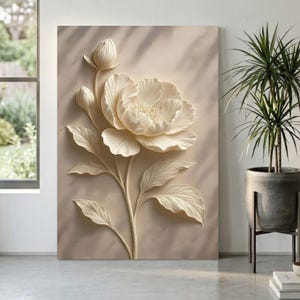 May include: A cream-colored floral wall art piece featuring a large, detailed peony with leaves and buds. The artwork is mounted on a neutral-toned background, creating a three-dimensional effect. The piece is displayed in a well-lit room with a potted plant.