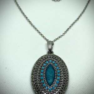 May include: A silver chain necklace with a pendant featuring a turquoise oval stone surrounded by a silver circle design.