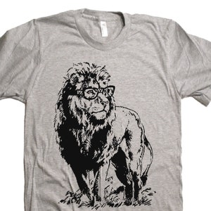 May include: A gray t-shirt with a black and white illustration of a lion wearing glasses. The lion is standing in a grassy field.