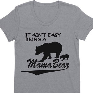 May include: A heather gray t-shirt with a crew neck. The shirt features the text "IT AIN'T EASY BEING A Mama Bear" in black, along with a silhouette of a bear and a cub. The brand name "LAST EARTH" is printed at the bottom.