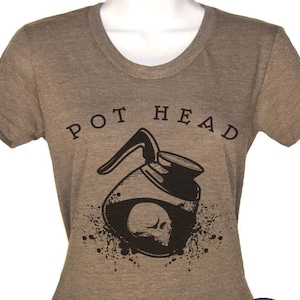 Puede incluir: Una camiseta marr&oacute;n con un gr&aacute;fico negro de una cafetera con una calavera en su interior. El texto "POT HEAD" est&aacute; impreso sobre el gr&aacute;fico. La camiseta es de la marca "Last Earth Clothing."