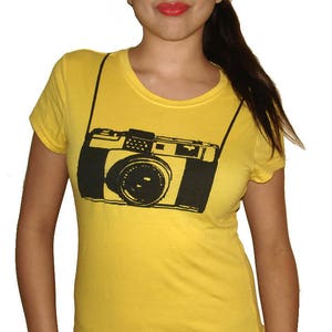 May include: A yellow t-shirt with a black and white graphic of a camera with a strap.