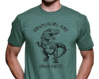 May include: A teal green t-shirt with a black and white illustration of a dinosaur. The text "Dinosaurs are Dino-mite!" is printed on the shirt.