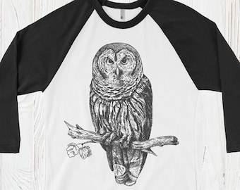May include: A white and black baseball tee shirt with a black and white illustration of an owl perched on a branch. The shirt has a black collar and black sleeves.