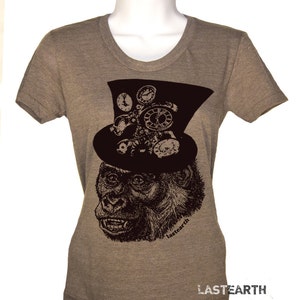Puede incluir: Camiseta gris jaspeado con un gorila que lleva un sombrero de copa negro adornado con relojes y engranajes. El texto "lastearth" está impreso en la camiseta, con el nombre de la marca repetido en la parte inferior.