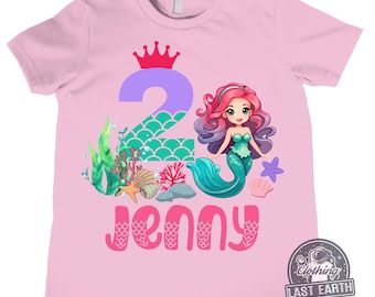 May include: Pink t-shirt with a mermaid graphic and the number 2. The mermaid is wearing a crown and holding a seashell. The text "Jenny" is written below the graphic.