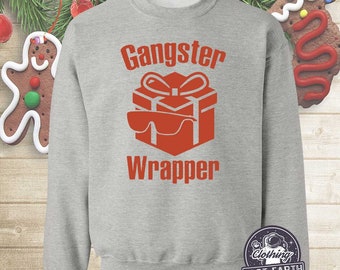 Pode incluir: Uma camisa de frio cinza com o texto "Gangster Wrapper" em vermelho. Uma caixa de presente vermelha com óculos de sol está acima do texto.