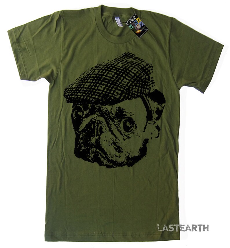 Pode incluir: Uma camiseta verde com um gr&aacute;fico preto e branco de um pug usando um bon&eacute; plano. O texto "LASTEARTH" est&aacute; impresso no canto inferior direito da camiseta.