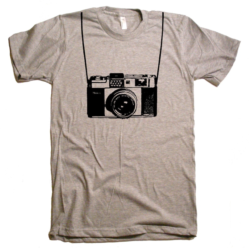 May include: A heather grey t-shirt with a black and white illustration of a vintage camera hanging from a strap.