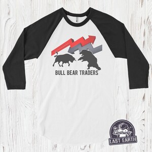 Puede incluir: Una camiseta de estilo b&eacute;isbol blanca y negra con un gr&aacute;fico de toro y oso rojo y gris. El texto "BULL BEAR TRADERS" est&aacute; impreso debajo del gr&aacute;fico.