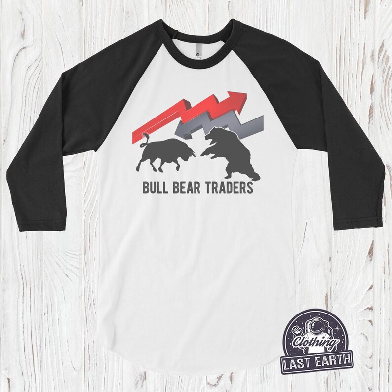 Puede incluir: Una camiseta de estilo b&eacute;isbol blanca y negra con un gr&aacute;fico de toro y oso rojo y gris. El texto "BULL BEAR TRADERS" est&aacute; impreso debajo del gr&aacute;fico.