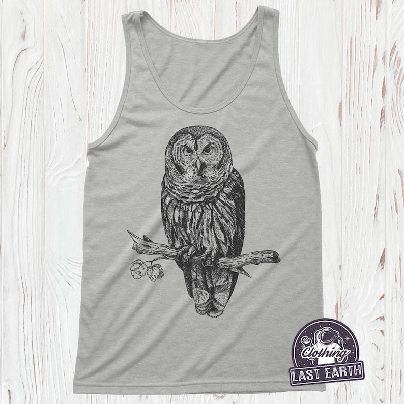 May include: A gray tank top with a black and white illustration of an owl perched on a branch. The owl has large, round eyes and a detailed feather pattern. The branch has a few leaves on it.