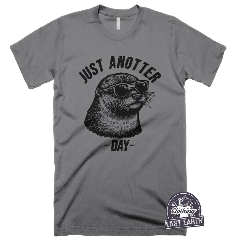 May include: Gray t-shirt with a black and white illustration of an otter wearing sunglasses. The text "Just Anotter Day" is printed on the shirt.