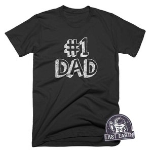 May include: Black t-shirt with white text that reads "#1 DAD" in a handwritten style.