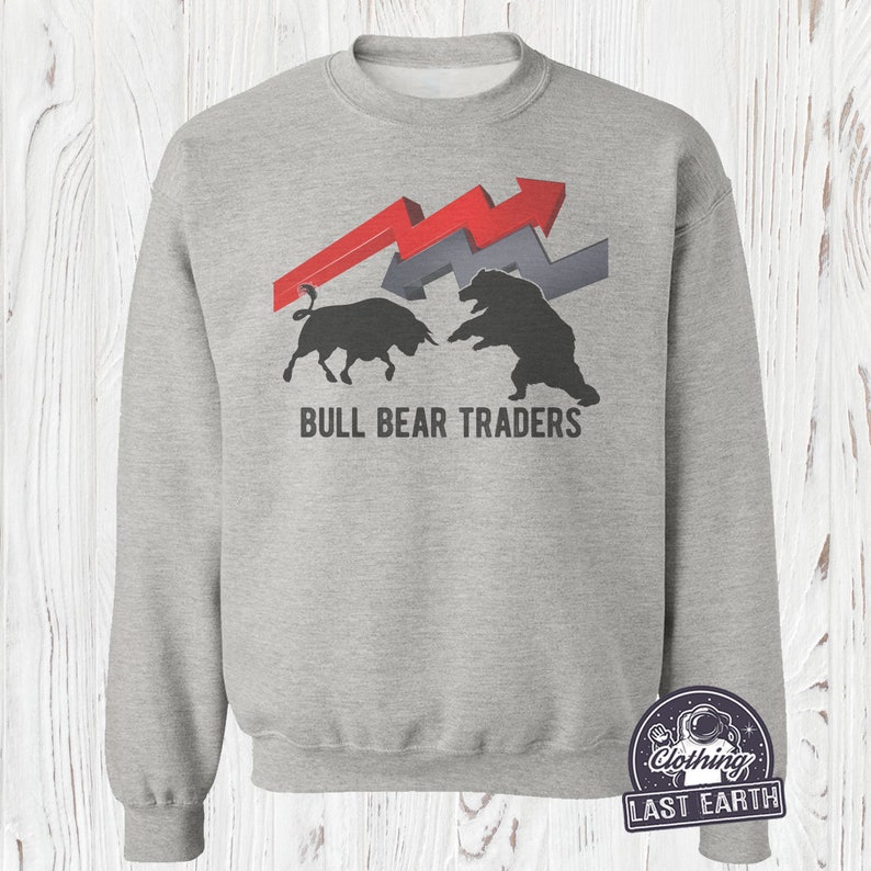 Puede incluir: Una sudadera gris con un gr&aacute;fico de un toro y un oso enfrentados con flechas apuntando hacia arriba y hacia abajo. El texto "BULL BEAR TRADERS" est&aacute; impreso debajo del gr&aacute;fico.