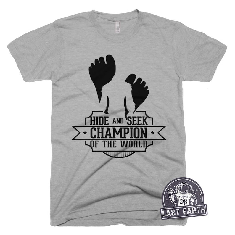 May include: Gray t-shirt with a black silhouette of a person with raised fists and the text "Hide and Seek Champion of the World".