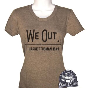 Puede incluir: Una camiseta marr&oacute;n con el texto "We Out." y la cita "Harriet Tubman, 1849" impresa en ella. La camiseta est&aacute; hecha por Last Earth Clothing.
