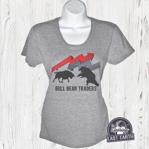 Puede incluir: Camiseta gris con un gr&aacute;fico de un toro y un oso enfrentados con flechas rojas y grises. El texto "BULL BEAR TRADERS" est&aacute; impreso debajo del gr&aacute;fico.