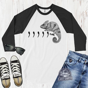 Peut inclure: Un t-shirt de baseball blanc et noir avec un graphique de cam&eacute;l&eacute;on noir et le texte ",,,,," imprim&eacute; sur le devant. Le t-shirt a des manches noires et un corps blanc.