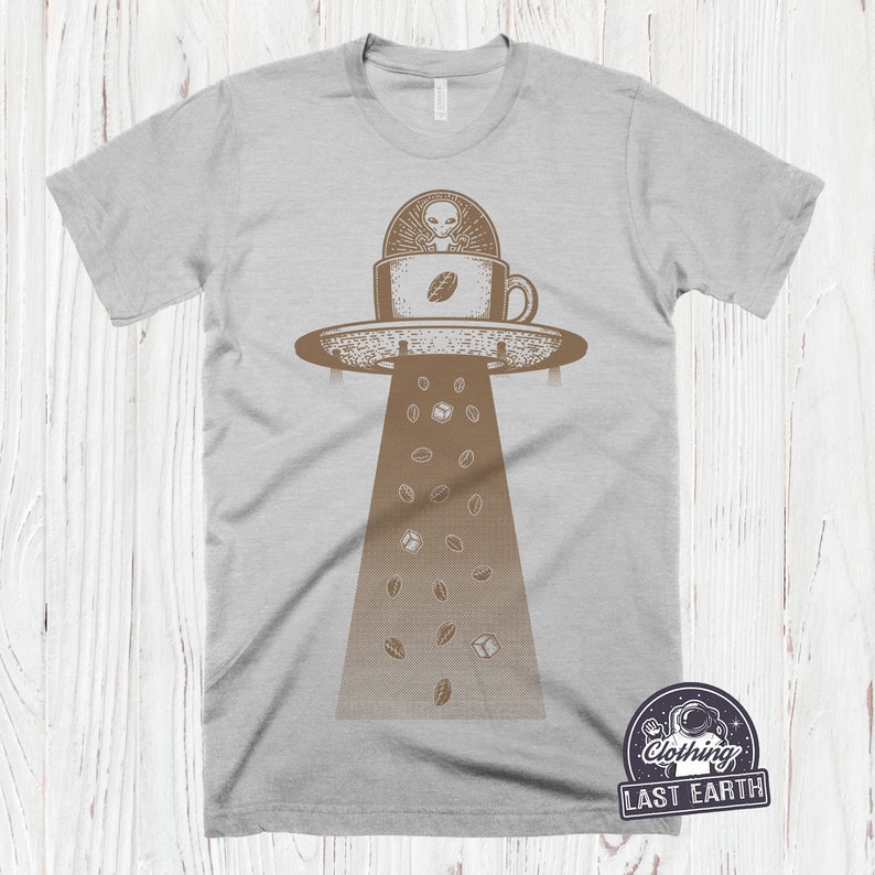 May include: A gray t-shirt with a graphic of a UFO holding a coffee cup with an alien inside. Coffee beans and sugar cubes fall from the UFO. The text "Last Earth" is on the bottom right corner of the shirt.