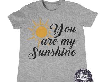 Może przedstawiać: Szara koszulka z żółtym nadrukiem słońca i tekstem "You are my Sunshine".