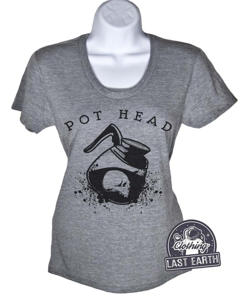 Puede incluir: Camiseta gris con un gr&aacute;fico en blanco y negro de una cafetera con una calavera en su interior. El texto "POT HEAD" est&aacute; por encima del gr&aacute;fico. La camiseta es de Last Earth Clothing.