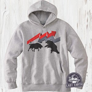 Puede incluir: Una sudadera con capucha gris con un gr&aacute;fico de un toro y un oso enfrentados. El toro es negro y el oso es negro. El gr&aacute;fico est&aacute; sobre un fondo de flechas rojas y grises. La sudadera tiene un bolsillo canguro y una capucha con cord&oacute;n. El texto "Last Earth Clothing" est&aacute; impreso en la esquina inferior derecha de la sudadera.