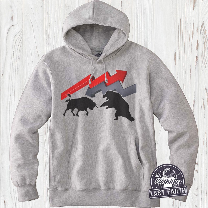 Puede incluir: Una sudadera con capucha gris con un gr&aacute;fico de un toro y un oso enfrentados. El toro es negro y el oso es negro. El gr&aacute;fico est&aacute; sobre un fondo de flechas rojas y grises. La sudadera tiene un bolsillo canguro y una capucha con cord&oacute;n. El texto "Last Earth Clothing" est&aacute; impreso en la esquina inferior derecha de la sudadera.