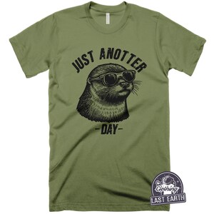 May include: A green t-shirt with a black graphic of an otter wearing sunglasses and the text "Just Anotter Day".