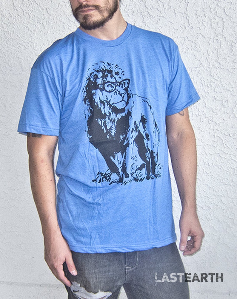 May include: A blue t-shirt with a black and white graphic of a lion wearing glasses. The lion is facing to the right and has a mane.