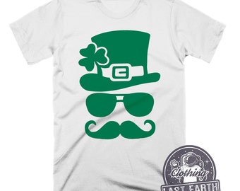Puede incluir: Camiseta blanca con un gráfico de cara de duende verde. El duende lleva un sombrero, gafas de sol y un bigote.