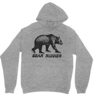 Puede incluir: Una sudadera con capucha gris con un oso negro que lleva zapatillas y el texto "BEAR RUNNER" impreso en la parte delantera.
