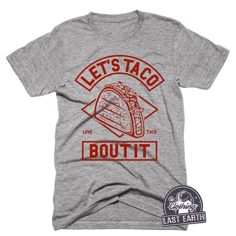 Puede incluir: Camiseta gris con un gr&aacute;fico rojo de un taco y el texto "Let's Taco Bout It".