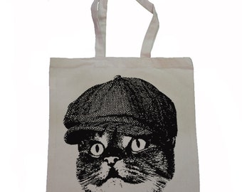 May include: A white tote bag with a black and white illustration of a cat wearing a flat cap. The cat has large eyes and a serious expression.