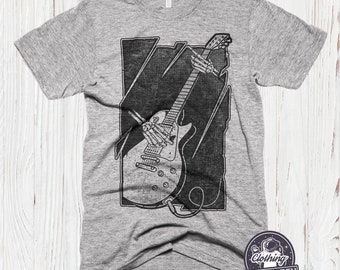 May include: A gray t-shirt with a black and white graphic of a skeleton playing an electric guitar. The graphic is in a rectangular frame with a distressed look. The t-shirt has the text "Clothing Last Earth" in a circle with a star and an astronaut graphic.