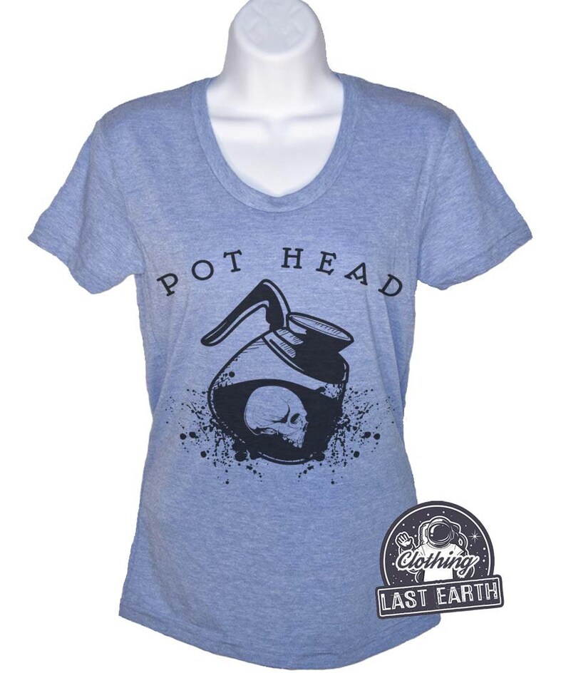 Puede incluir: Una camiseta azul claro con un gr&aacute;fico negro de una cafetera con una calavera en su interior. El texto "POT HEAD" est&aacute; impreso sobre el gr&aacute;fico. La camiseta es de la marca "Last Earth Clothing."