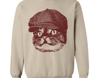 May include: A beige sweatshirt with a maroon cat wearing a newsboy cap. The cat's eyes are wide open and it has a serious expression.
