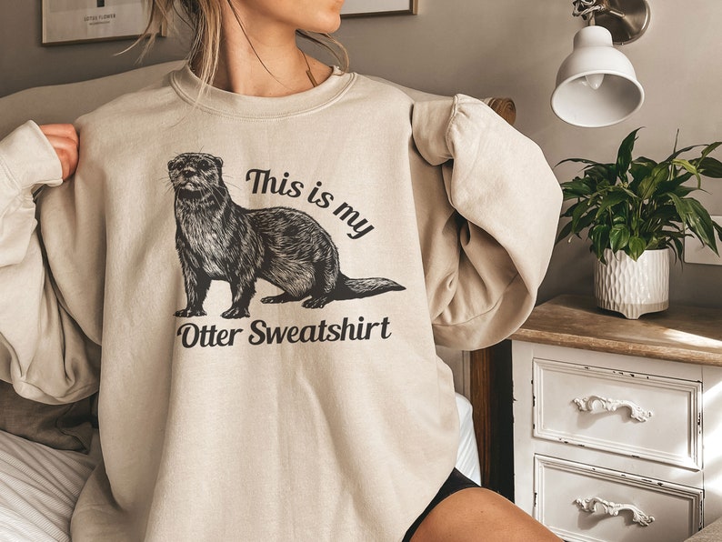 May include: A beige sweatshirt with a black and white illustration of an otter and the text "This is my Otter Sweatshirt".