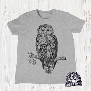 May include: A gray t-shirt with a black and white illustration of an owl perched on a branch. The owl has large, round eyes and detailed feathers. The t-shirt has the text "Clothing Last Earth" in a circle with a spaceman graphic.