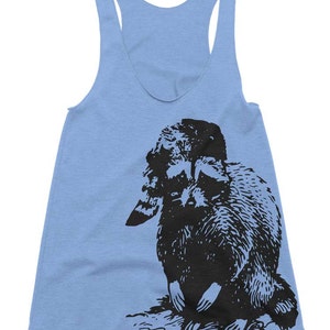 May include: A light blue tank top with a black and white illustration of a raccoon on the front.