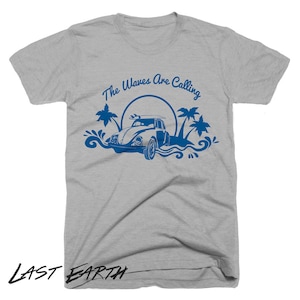 May include: A heather grey t-shirt with a blue graphic of a vintage car with a surfboard on top, palm trees, and the text "The Waves Are Calling".